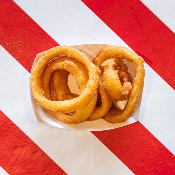 Golden-brown onion rings in a white paper tray, centered on a red and white striped background.