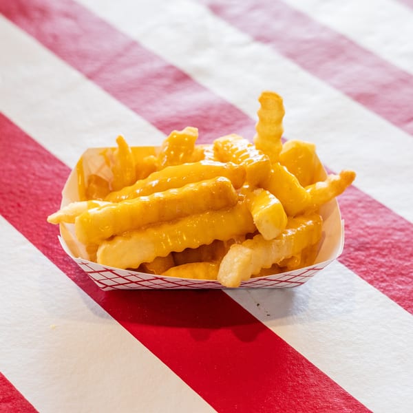 Crinkle-cut fries covered in melted cheese sauce, served in a paper tray on a red and white striped surface.