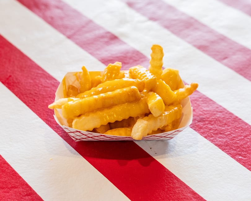 Crinkle-cut fries covered in melted cheese sauce, served in a paper tray on a red and white striped surface.