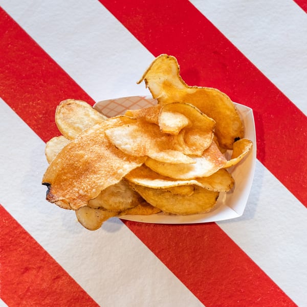 Crispy golden potato chips in a white paper tray, centered on a red and white striped surface.