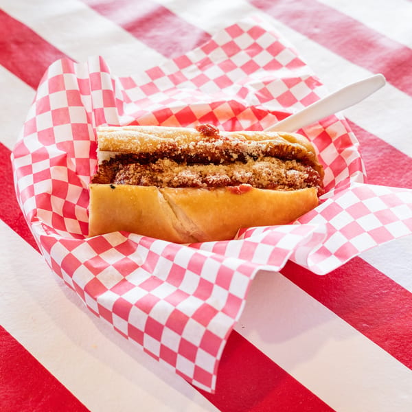 Meatball sub with red sauce and parmesan cheese, served in checkered paper on a striped table.