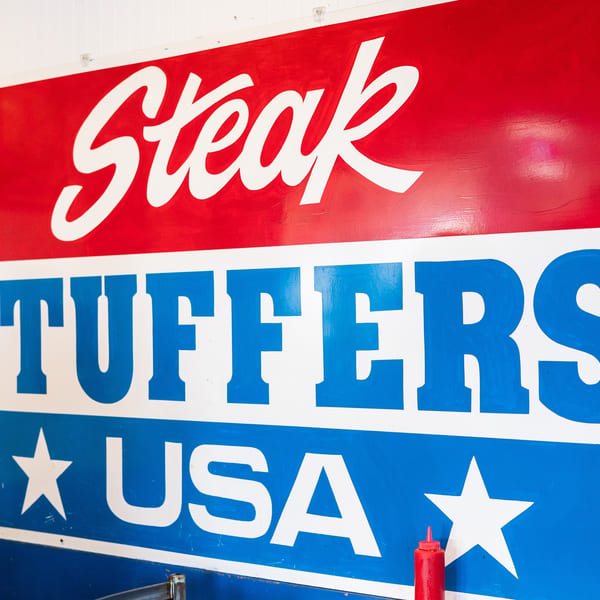 Red, white, and blue sign for "Steak Stuffers USA" with a red ketchup bottle below.