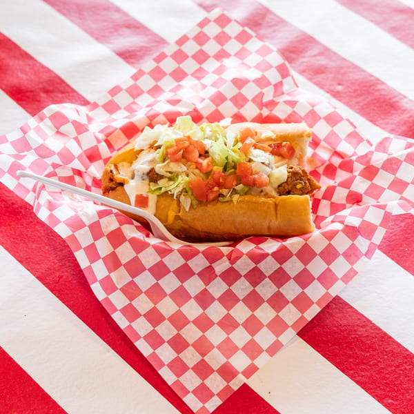 A fried chicken po'boy sandwich with lettuce, tomatoes, and sauce in a red and white checkered wrapper.