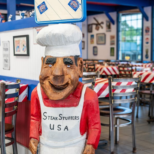 A wooden chef statue with "Steak Stuffers USA" on its apron stands in a restaurant dining room.