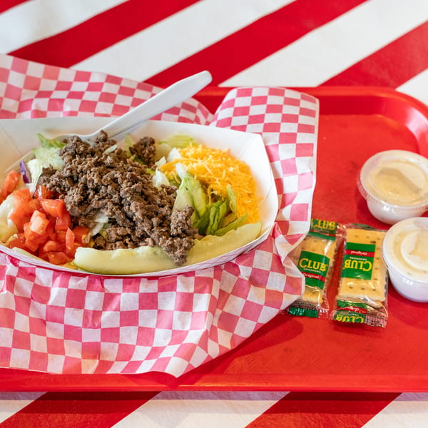 Taco salad with ground beef, lettuce, tomatoes, cheese, and pickles on a red tray.