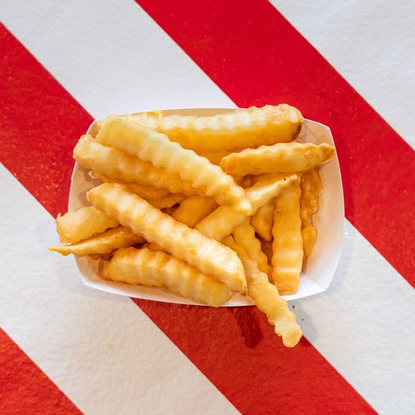 A white paper tray filled with golden, crinkle-cut french fries on a red and white striped surface.
