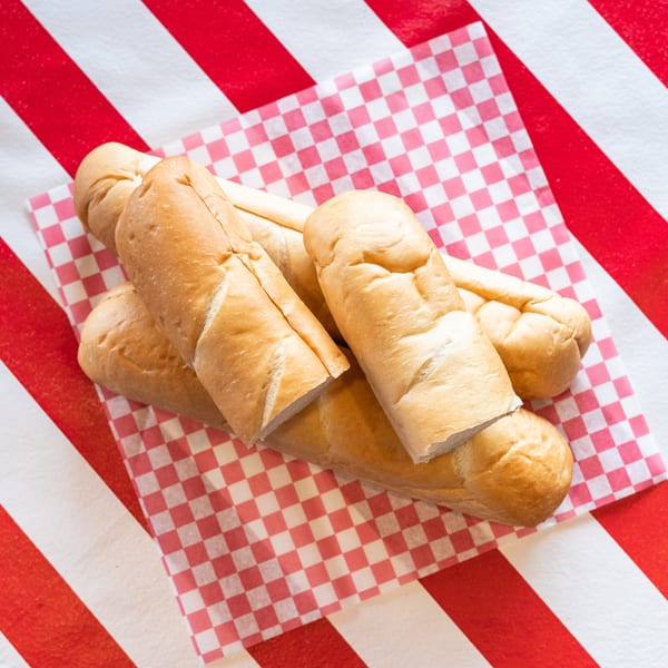 Freshly baked bread rolls on a red and white checkered paper, against a striped background.