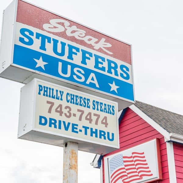 A red and blue sign for "Steak Stuffers USA" advertising "Philly Cheese Steaks" and a drive-thru.