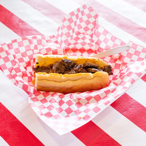Cheesesteak sandwich with melted cheese and steak in a red and white checkered wrapper on a striped table.