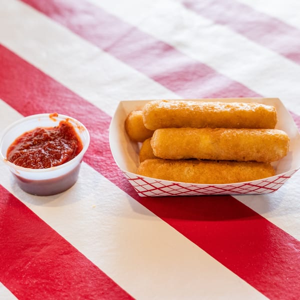 Golden-brown mozzarella sticks in a paper tray with a side of marinara sauce on a red and white striped table.