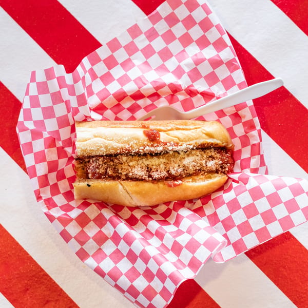 Meatball sub sandwich with sauce and cheese in red and white checkered paper on a striped table.