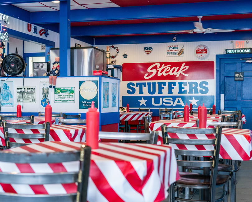 Interior of Steak Stuffers USA, with red and white striped tablecloths, blue walls, and patriotic decor.